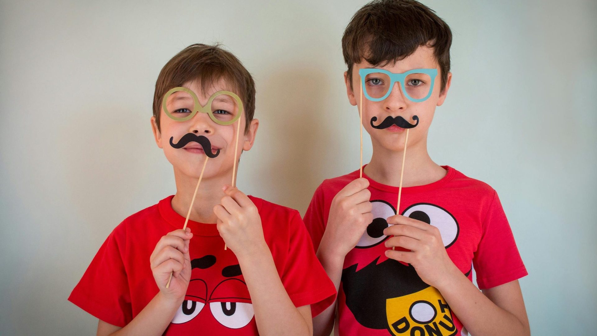 happy-two-young-males-in-party-glasses-and-party-mustache-looking-at-camera-while-standing-against-white-background-qZxr1oXLKpordtT1h6ocLQ